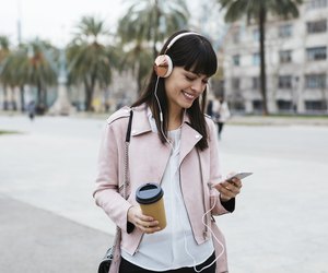 Spain, Barcelona, smiling woman with coffee, cell phone and headphones in the city
