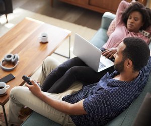 Couple Sitting On Sofa At Home Using Laptop Computer And Watching TV