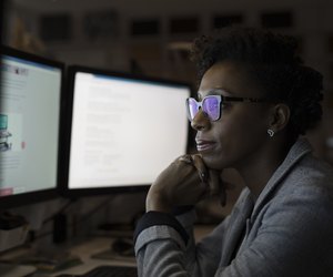 Focused, dedicated businesswoman working late at computers in dark office