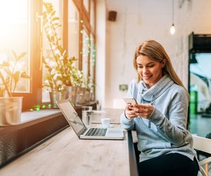 Woman using smartphone and laptop at a lovely bright cafe.