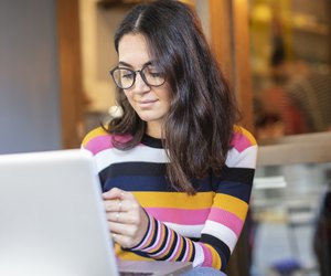 Beautiful Woman with Long Black Hair and Glasses Using a Laptop and Looking to Mobile Phone