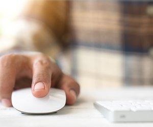 Male hand holding computer mouse with laptop keyboard in the background