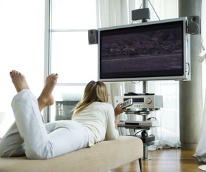 Female lying on chaise longue, watching flat screen television with surround sound