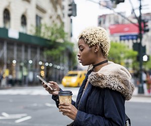 USA, New York City, fashionable young woman with coffee to go looking at cell phone on the street