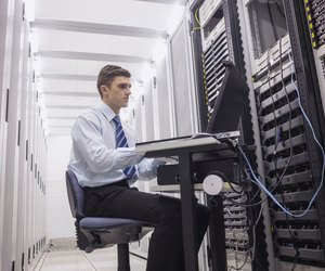 Technician sitting on swivel chair using laptop to diagnose servers