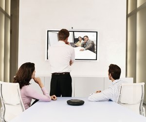 Businessmen and a Businesswoman Watching a Plasma Screen During a Video Conference Meeting