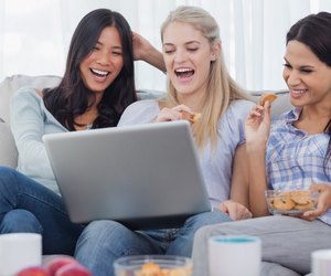 Laughing friends looking at laptop together and eating cookies
