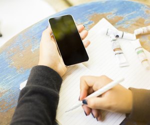 girl writes in notebook, with cell phone and ink drawing