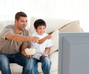 Happy father and son watching television while eating pop corn
