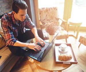Young man sitting at a cafe, using a laptop, drinking espresso