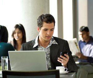 Young urban businessman using Blackberry PDA and wireless laptop in a hotspot cafe.