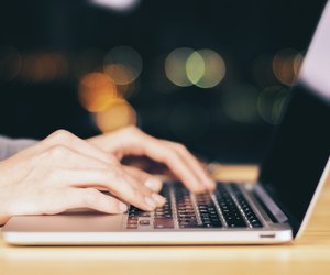 Girl hands typing on laptop on wooden table at night