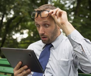Businessman at the park with tablet sitting on a bench.