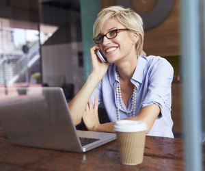 Businesswoman Using Phone Working On Laptop In Coffee Shop