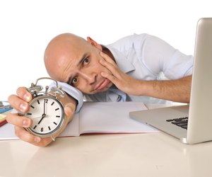 Overworked exhausted bald business man with computer and alarm clock