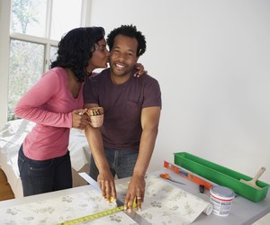 African man measuring wall paper getting kiss from wife