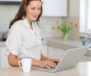 Smiling young woman using laptop in kitchen