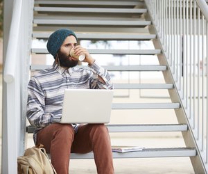 Young bearded hipster student using computer outdoors
