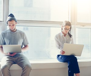 Man and woman with laptops near big bright window