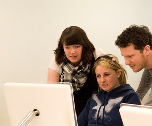 Group of three graphic design students working together on a mac computer.