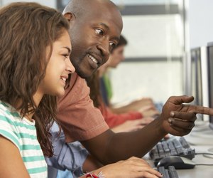 Teacher Helping Students Working At Computers In Classroom