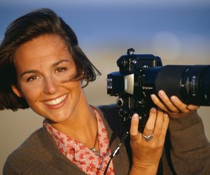 Woman holding camera with telephoto lens, smiling, portrait