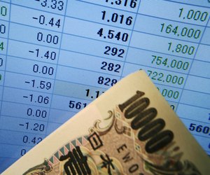 10, 100 Yen bill in front of computer screen displaying financial spreadsheet
