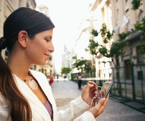 Businesswoman in street using hand held computer, smiling, close-up