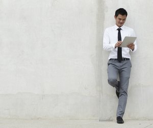 Young businessman reading while leaning on a blank wall