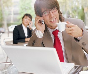 Businessman in cafe by laptop, using mobile phone