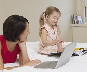 Mother and daughter drawing and using laptop on bed