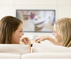 Two women in living room watching television eating chocolates