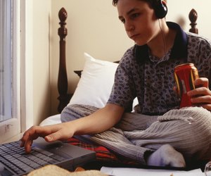 Teenage boy (16-17) using laptop, sitting on bed