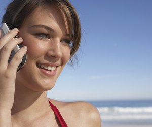 Young woman using mobile phone, outdoors, smiling, close-up