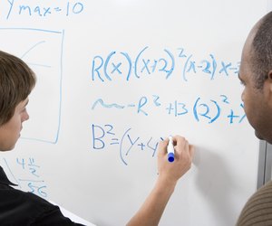 Student writing maths equations on whiteboard with tutor