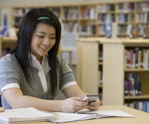 School girl (14-15) text messaging in library