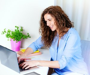 Smiling young woman siting at table and using laptop.