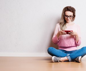 Happy beautiful woman sitting on the floor and using smartphone