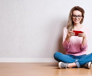 Happy beautiful woman sitting on the floor and using smartphone