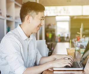 Handsome Asian man with computer in cafe (focus on face)
