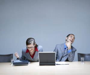 Businesswoman and businessman sitting at desk with laptop, laughing