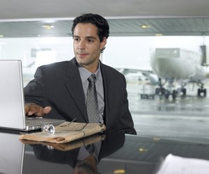 Businessman using laptop computer in airport, close-up