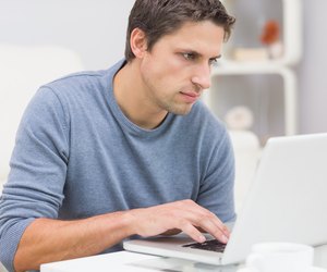 Serious young man using laptop in living room