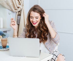 Cheerful woman using laptop and eating lollipop in cafe