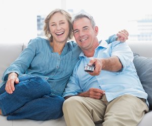 Cheerful couple cuddling and sitting on the couch watching tv