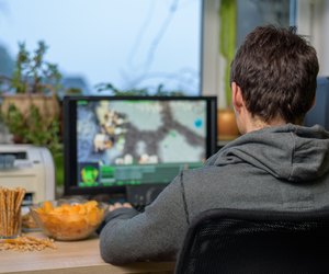 male gamer playing strategy game on computer eating snacks