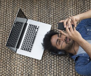 Asian man lying on the floor with laptop and phone.