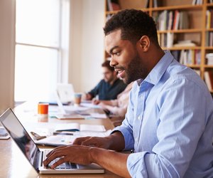 Businessman Using Laptop At Desk In Busy Office