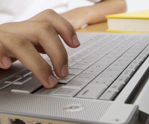Hand on computer keyboard with yellow book, close-up