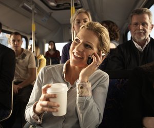 Woman using mobile phone on bus, smiling